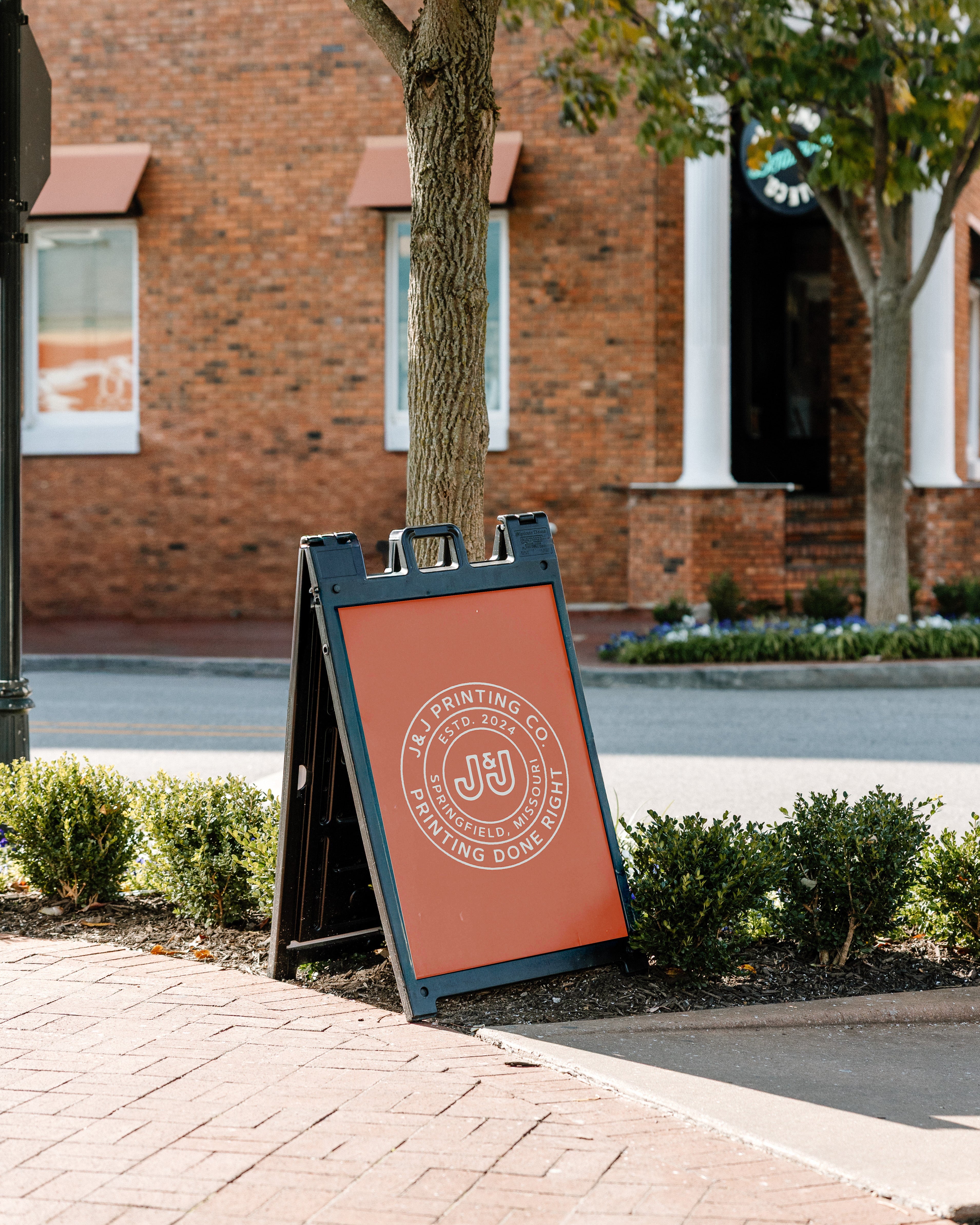 Outdoor sign with a logo on a sidewalk in front of a brick building